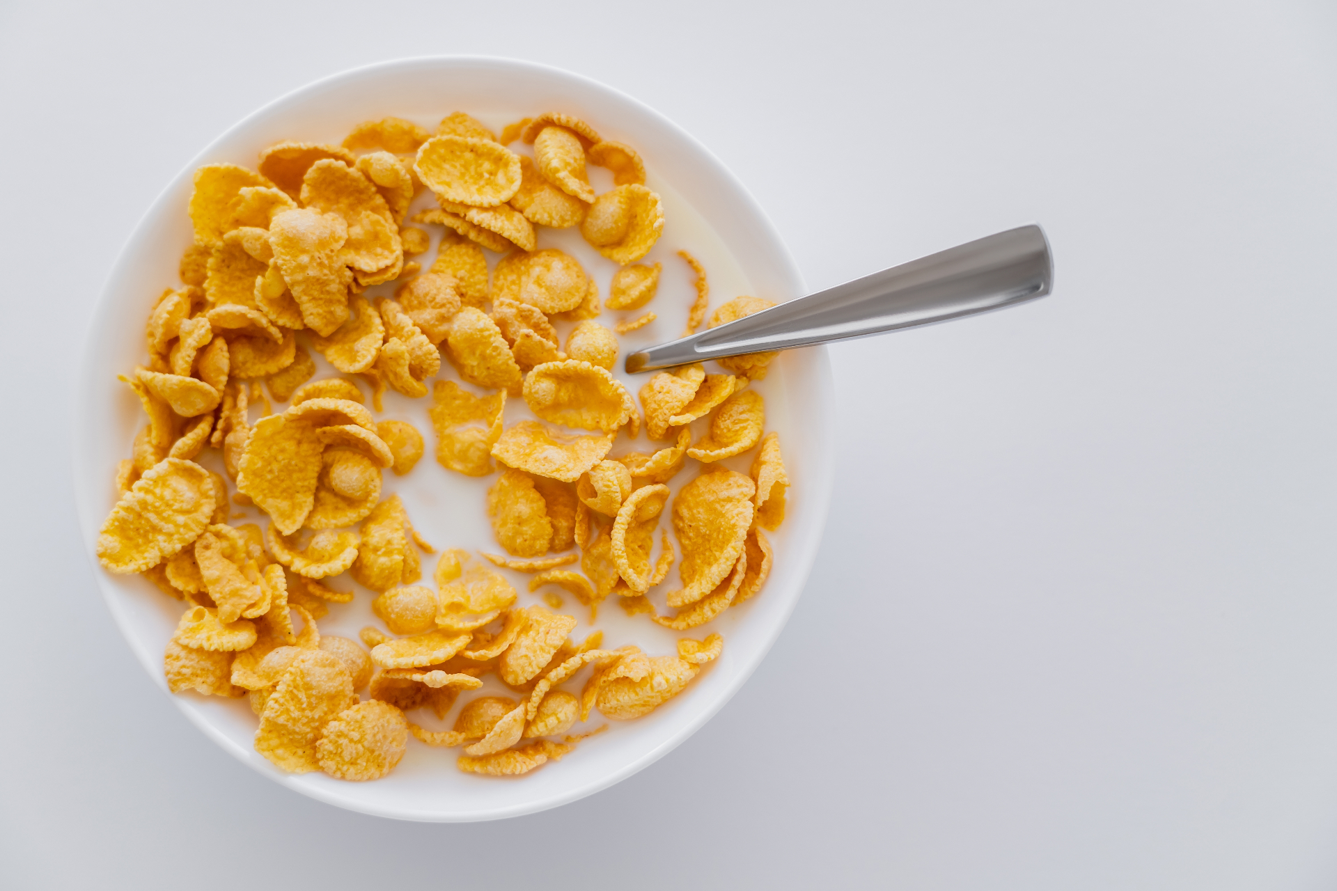 Overhead view of a bowl of cornflakes with milk and spoon